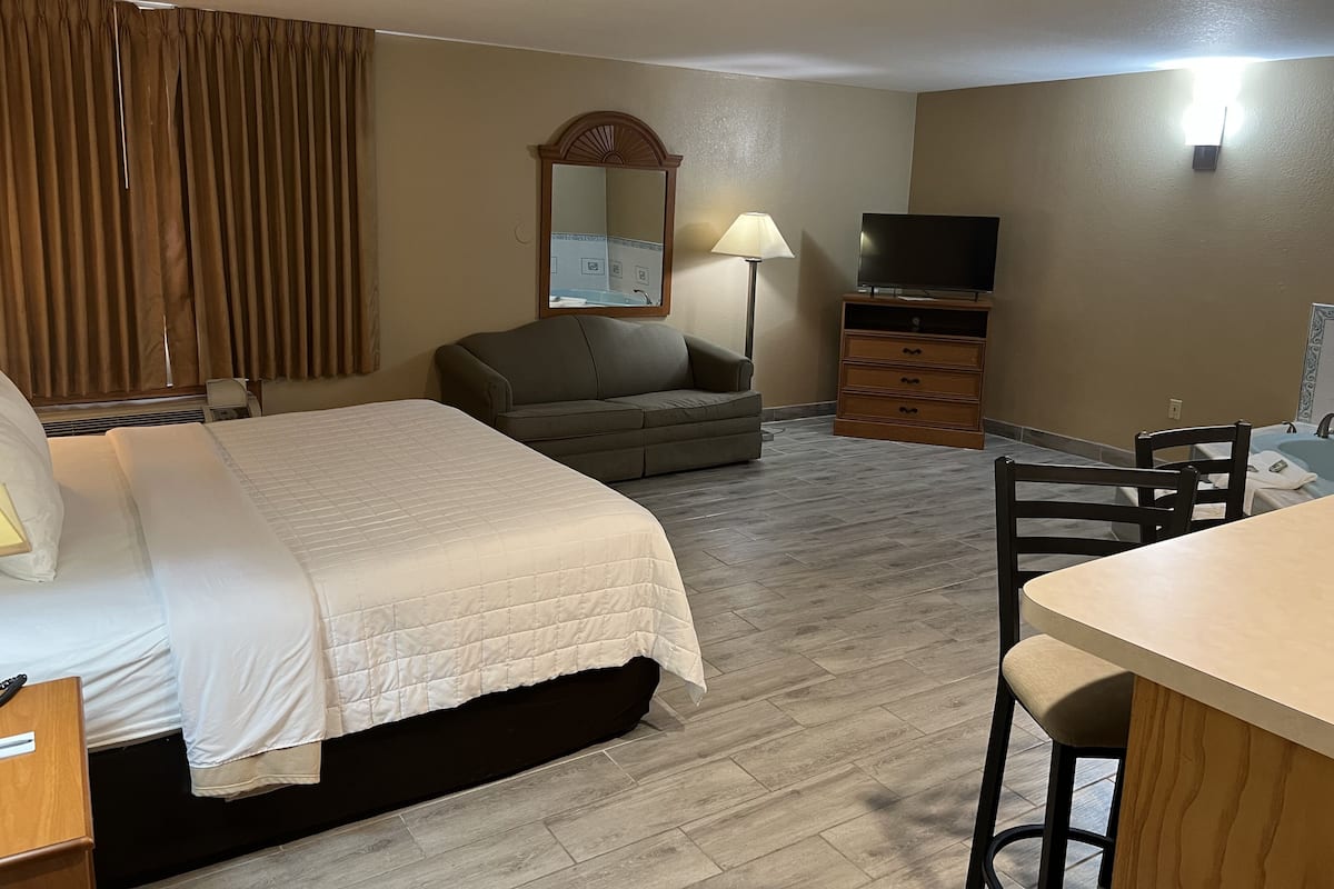 A hotel room with a bed, a sofa, a desk with a chair, a television, and a mirror.