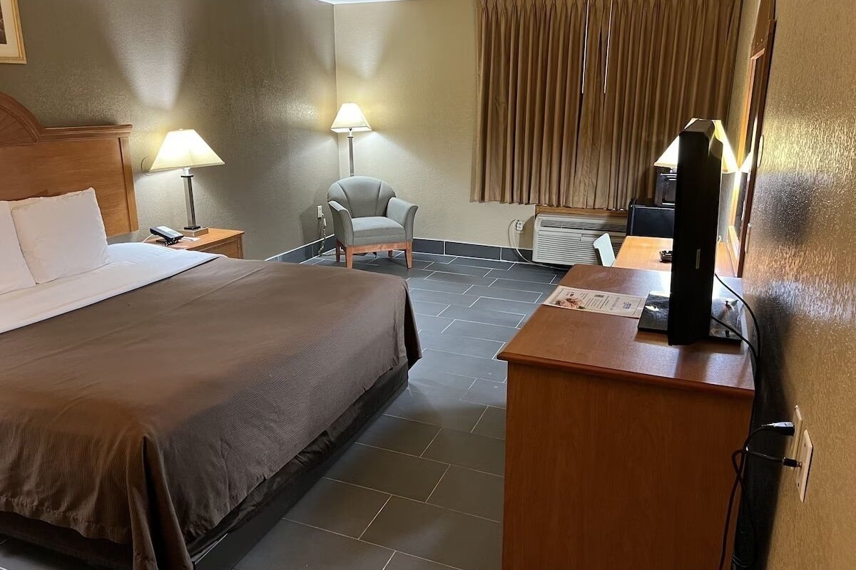 A hotel room with a bed, a desk, a chair, a lamp, and a television.