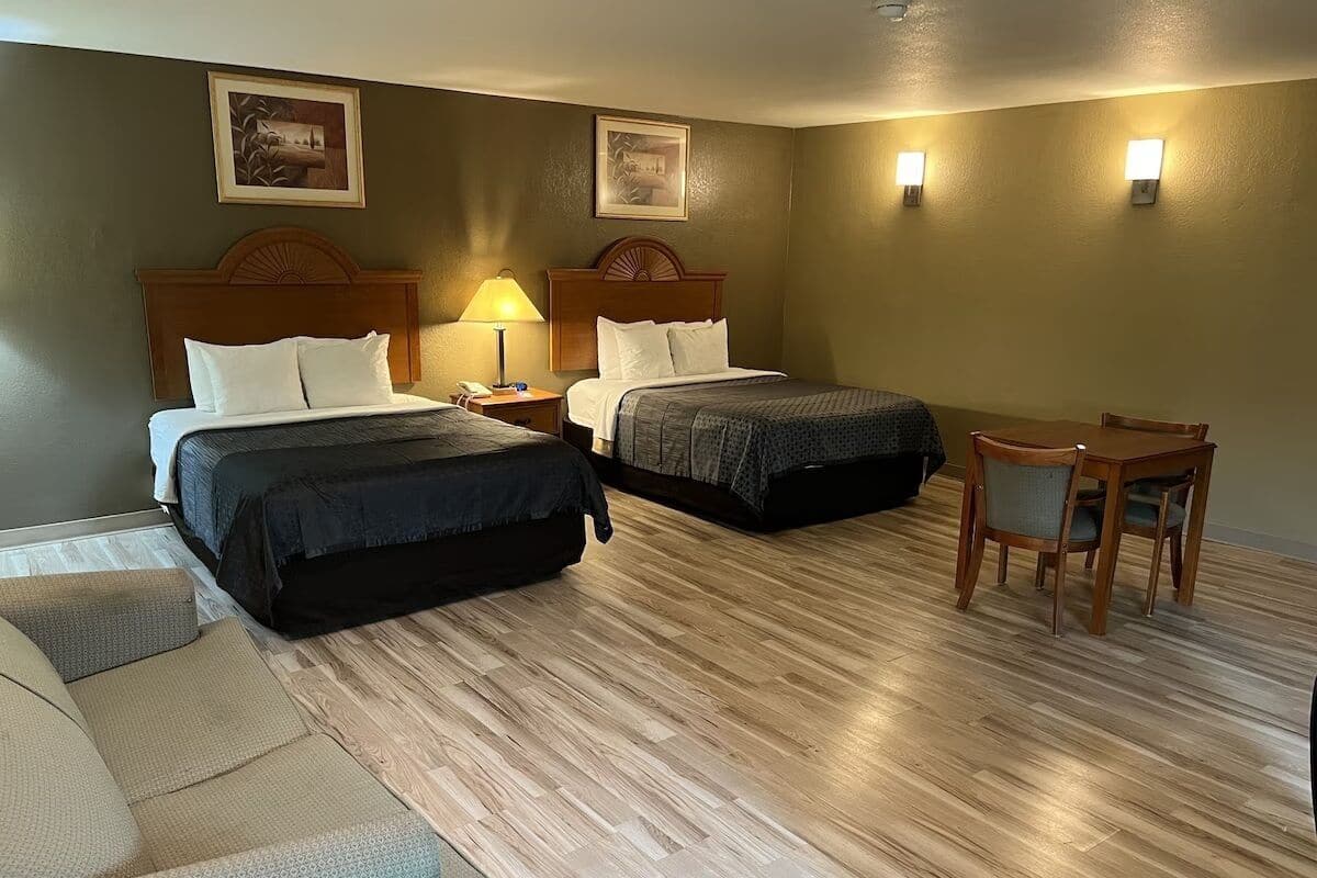 A hotel room with two beds, a small table, a chair, and two wall-mounted lamps.