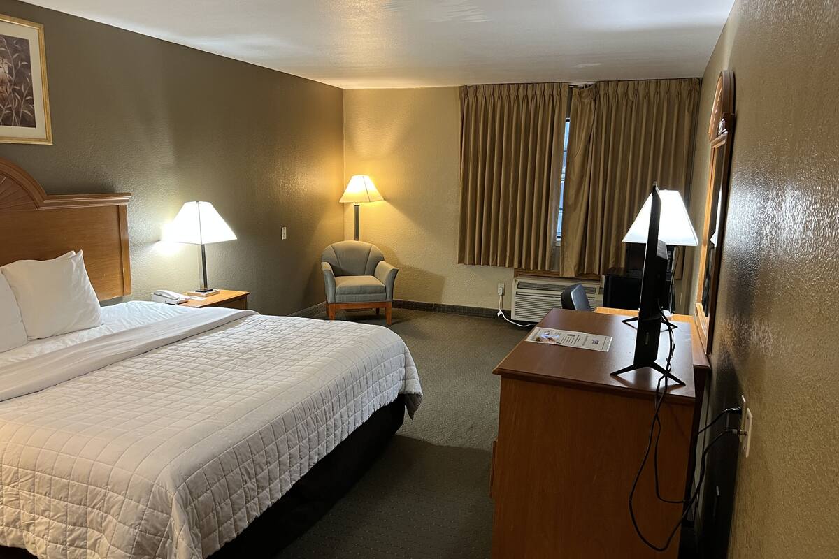 A hotel room with a bed, two bedside lamps, a chair, a desk with a computer, and a window with curtains.