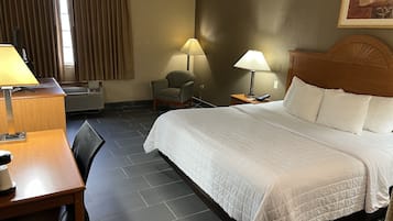 A hotel room with a bed, a desk, a chair, a lamp, and a painting on the wall.