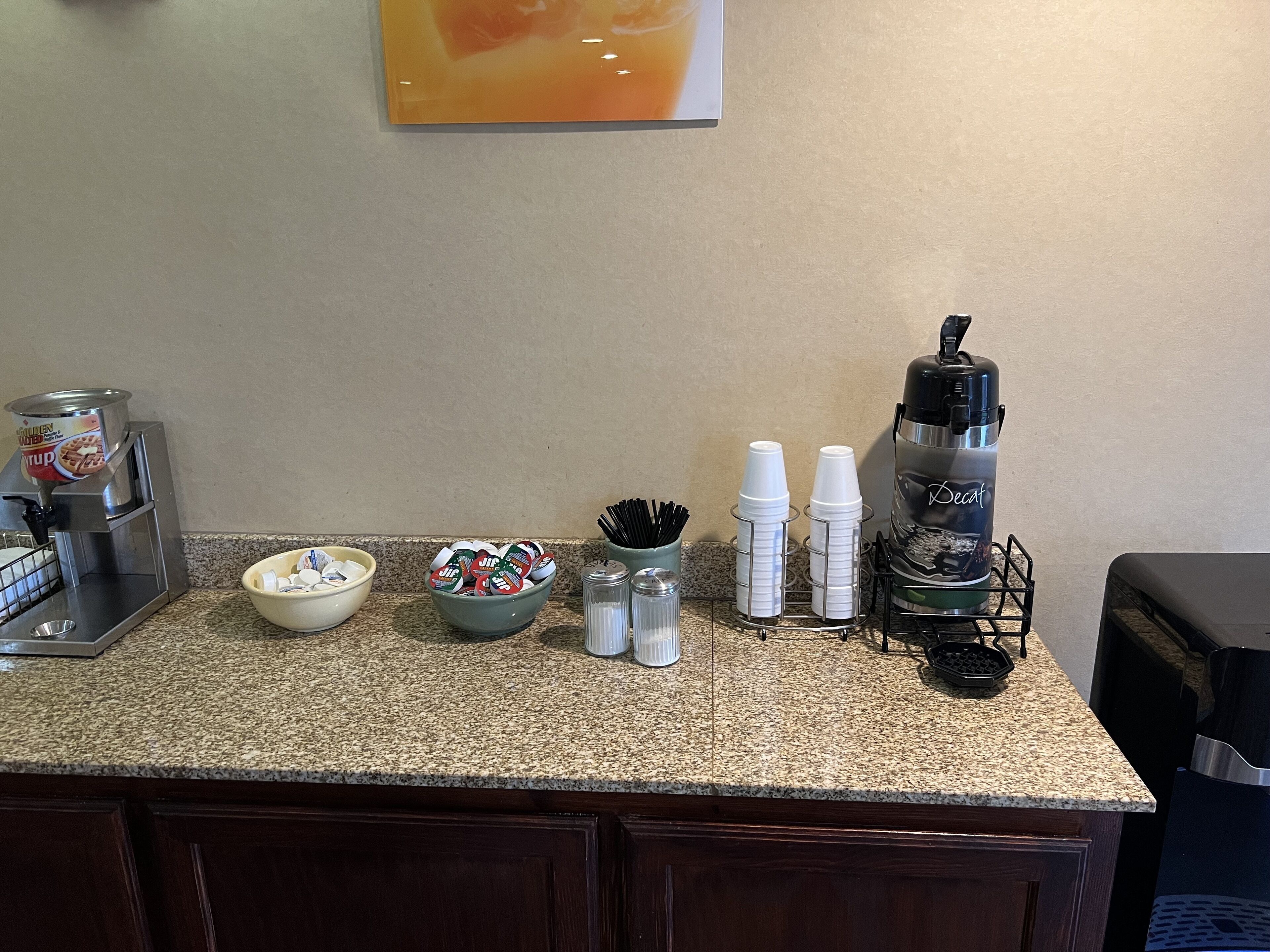 A kitchen counter with a waffle maker, a coffee machine, a bowl of waffles, and a coffee dispenser.