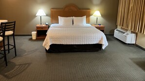 A hotel room with a large bed, two bedside tables with lamps, a chair, a waste bin, and a wall-mounted air conditioner. - Americas Best Value Inn Pharr (Pharr)