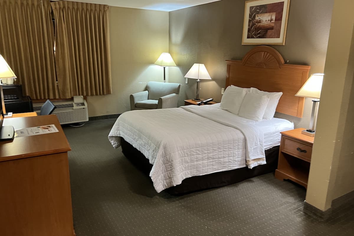 A hotel room with a large bed, two bedside tables with lamps, a chair, a desk, and a wall-mounted TV.