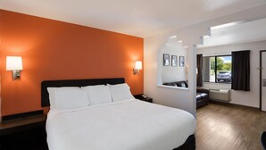 A hotel room with a large bed, two bedside lamps, a window with a view of the outside, and a small seating area with a sofa and a chair.
