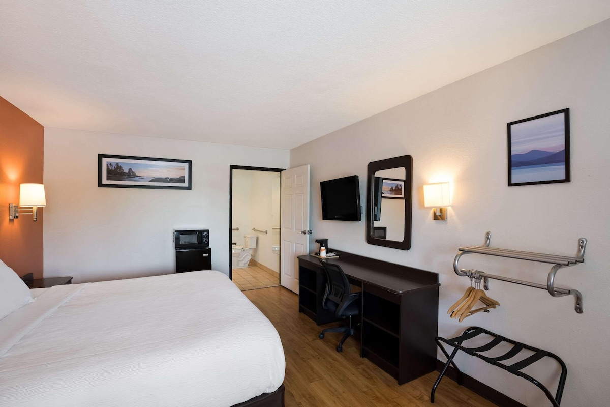 Quarto de hotel com cama, escrivaninha, cadeira e televisão fixada na parede.