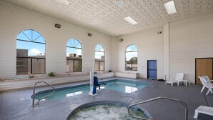 An indoor swimming pool with a hot tub, lounge chairs, and arched windows.