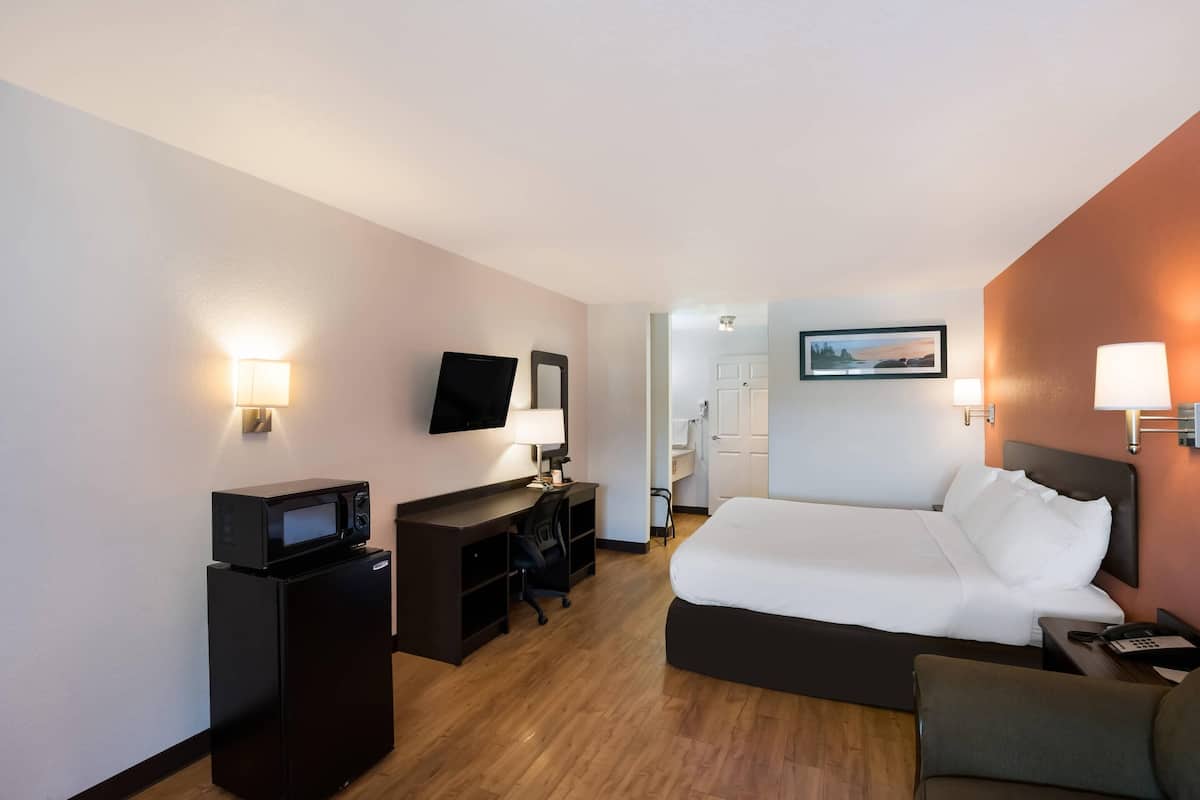 A hotel room with a bed, desk, chair, TV, and a microwave.