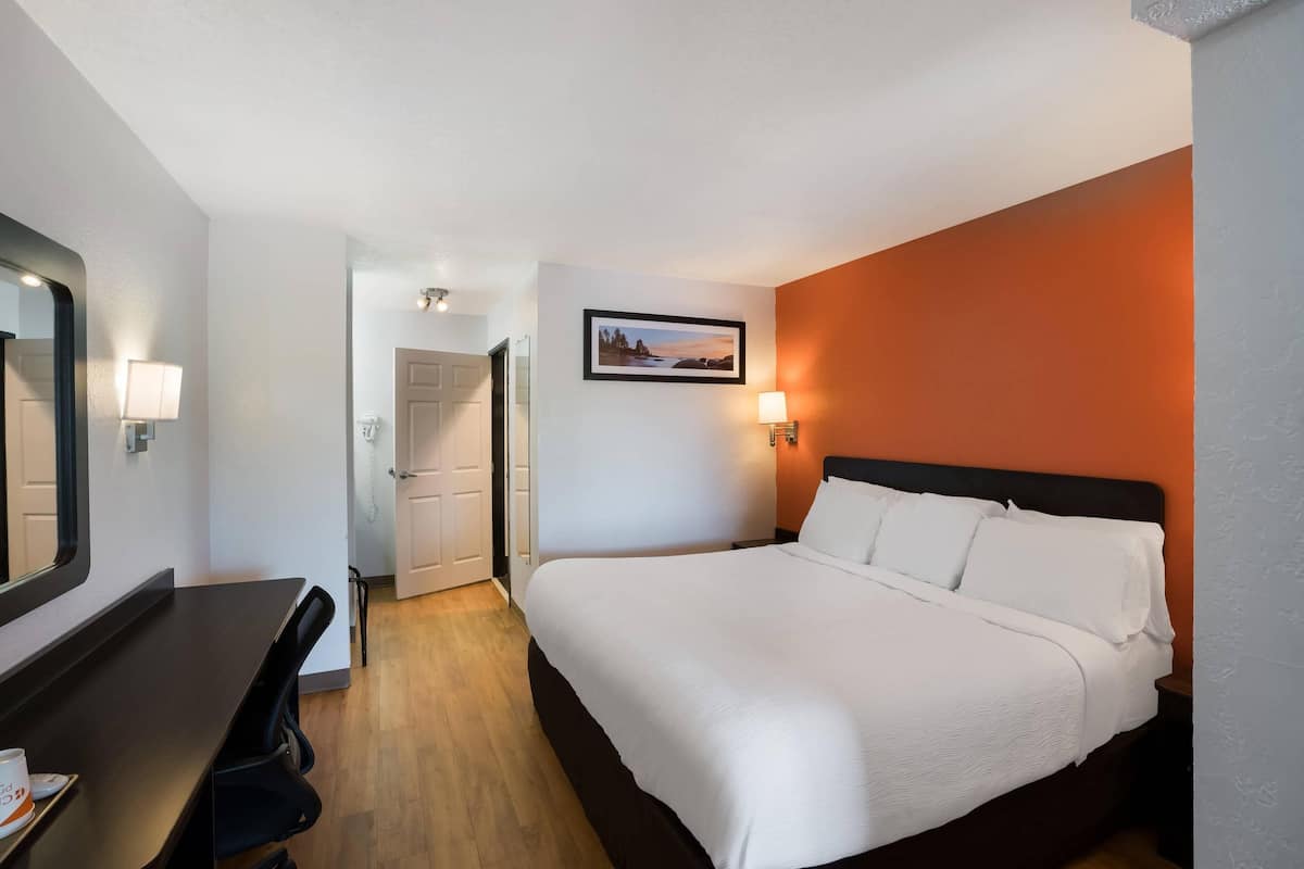 A hotel room with a bed, a desk, and a chair. There is a door leading to another room.