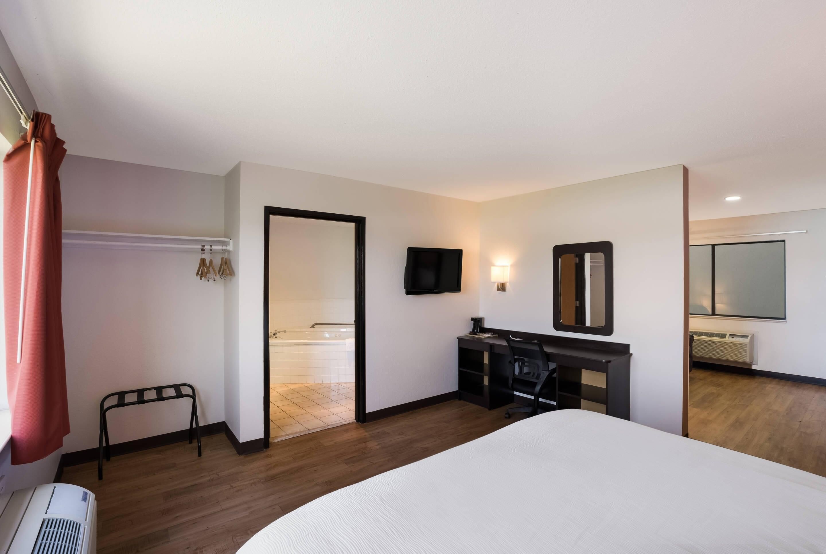 A hotel room with a bed, a desk with a chair, a TV, and a mirror.