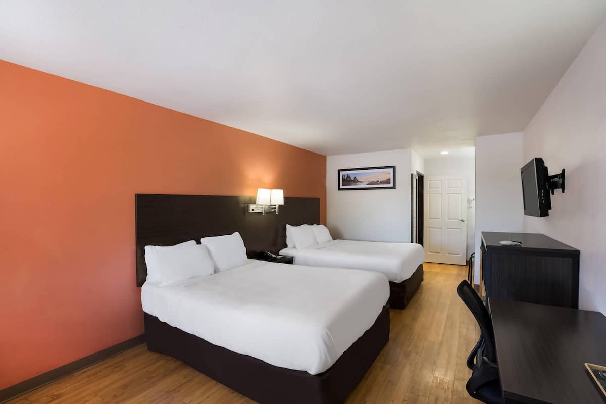 A hotel room with two beds, a desk, a chair, a TV, and a door leading to another room.