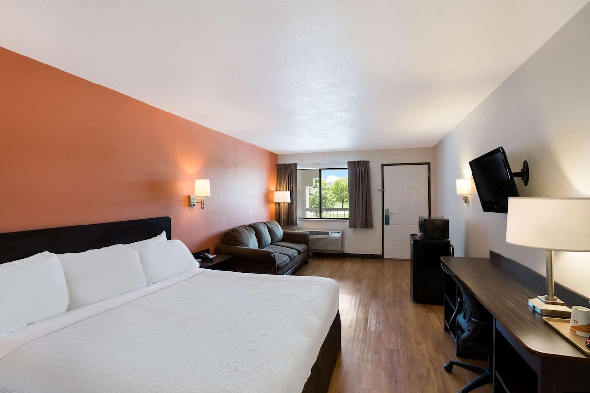 A hotel room with a large bed, a desk, a chair, a sofa, a TV, and a window with curtains.
