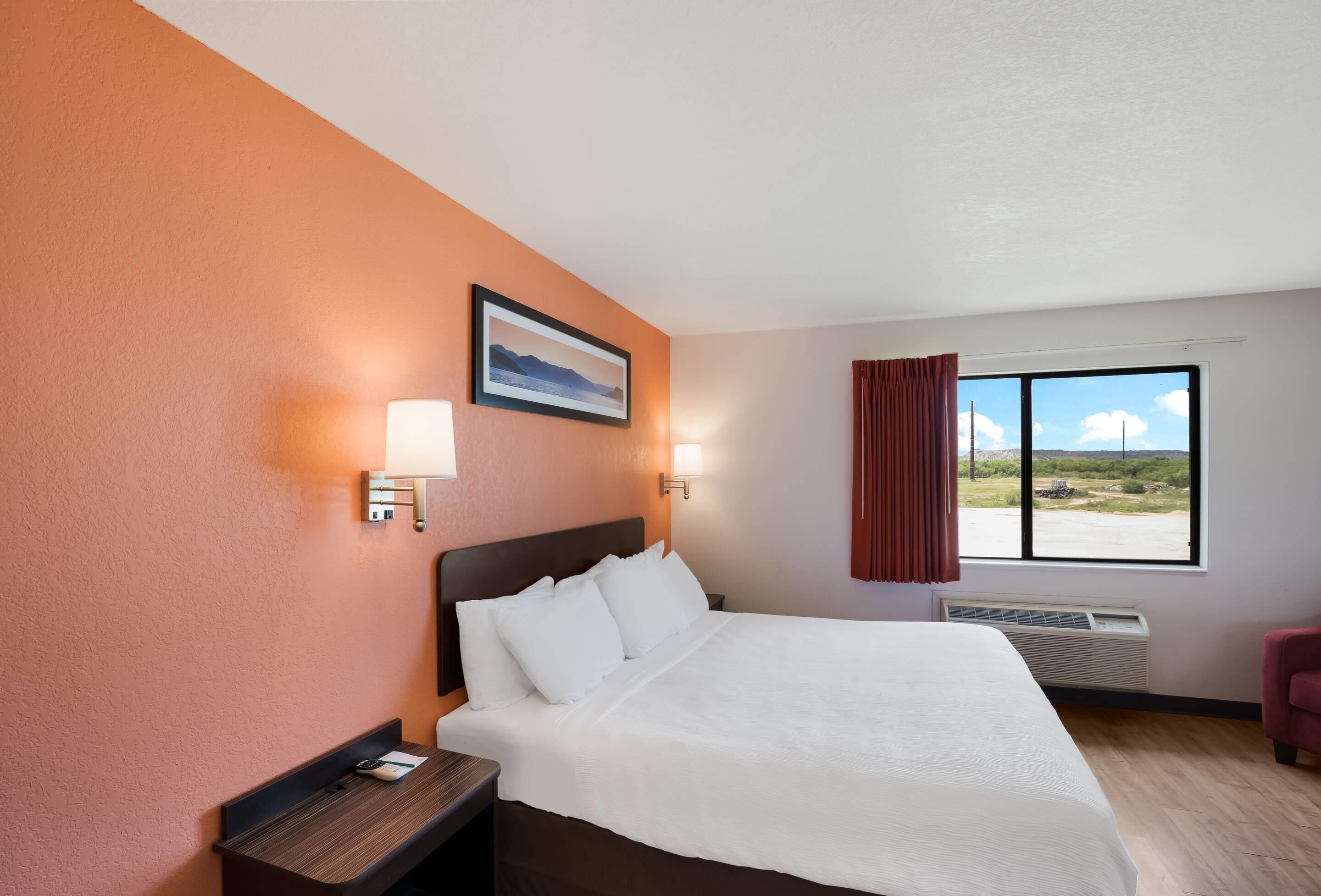 A hotel room with a large bed, two bedside lamps, a nightstand, a window with a view, and a framed picture on the wall.