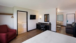 A hotel room with a bed, a desk with a chair, a red sofa, a TV, a mirror, and a bathroom visible through an open door.