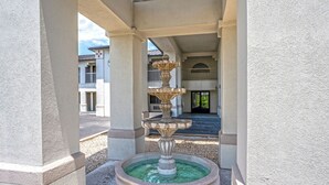 A stone fountain with a tiered design, located in a courtyard with a building in the background.