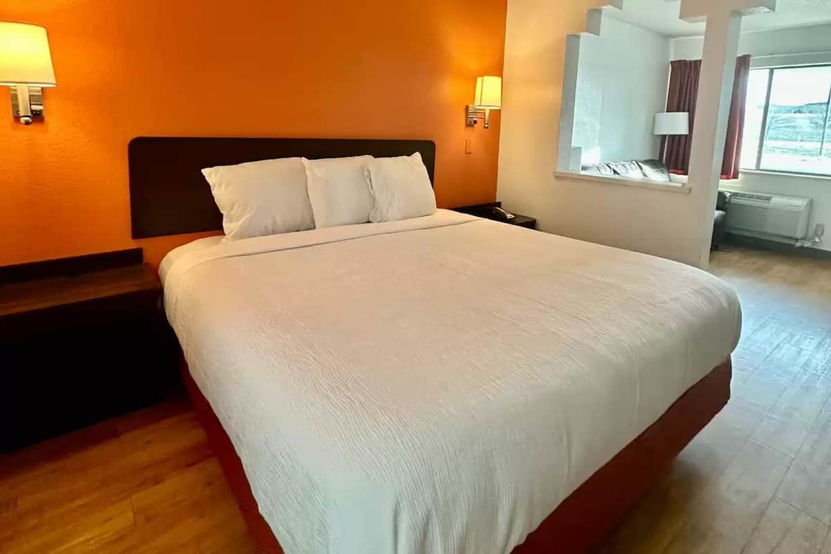 A hotel room with a large bed, two bedside lamps, a window with curtains, and a view of the outdoors.