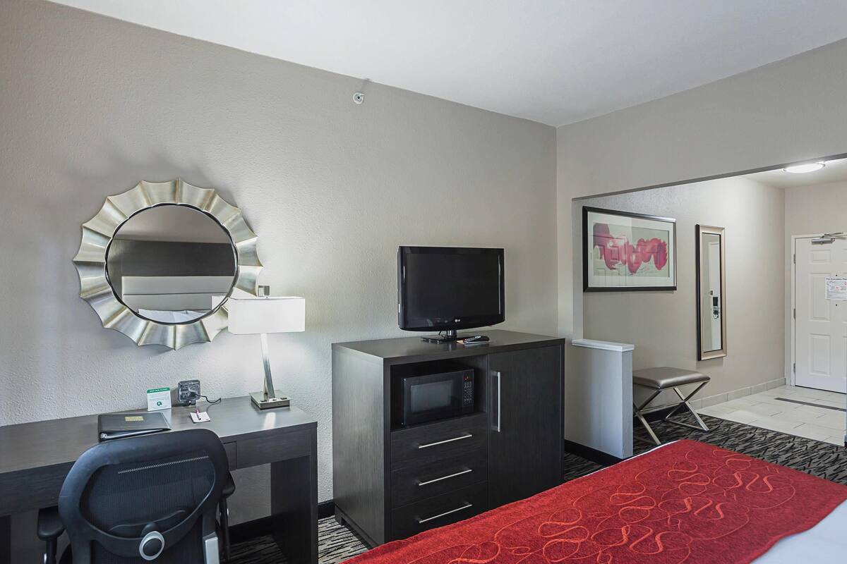 Hotelkamer met een bureau, stoel, televisie, magnetron en een bed met een rode deken.