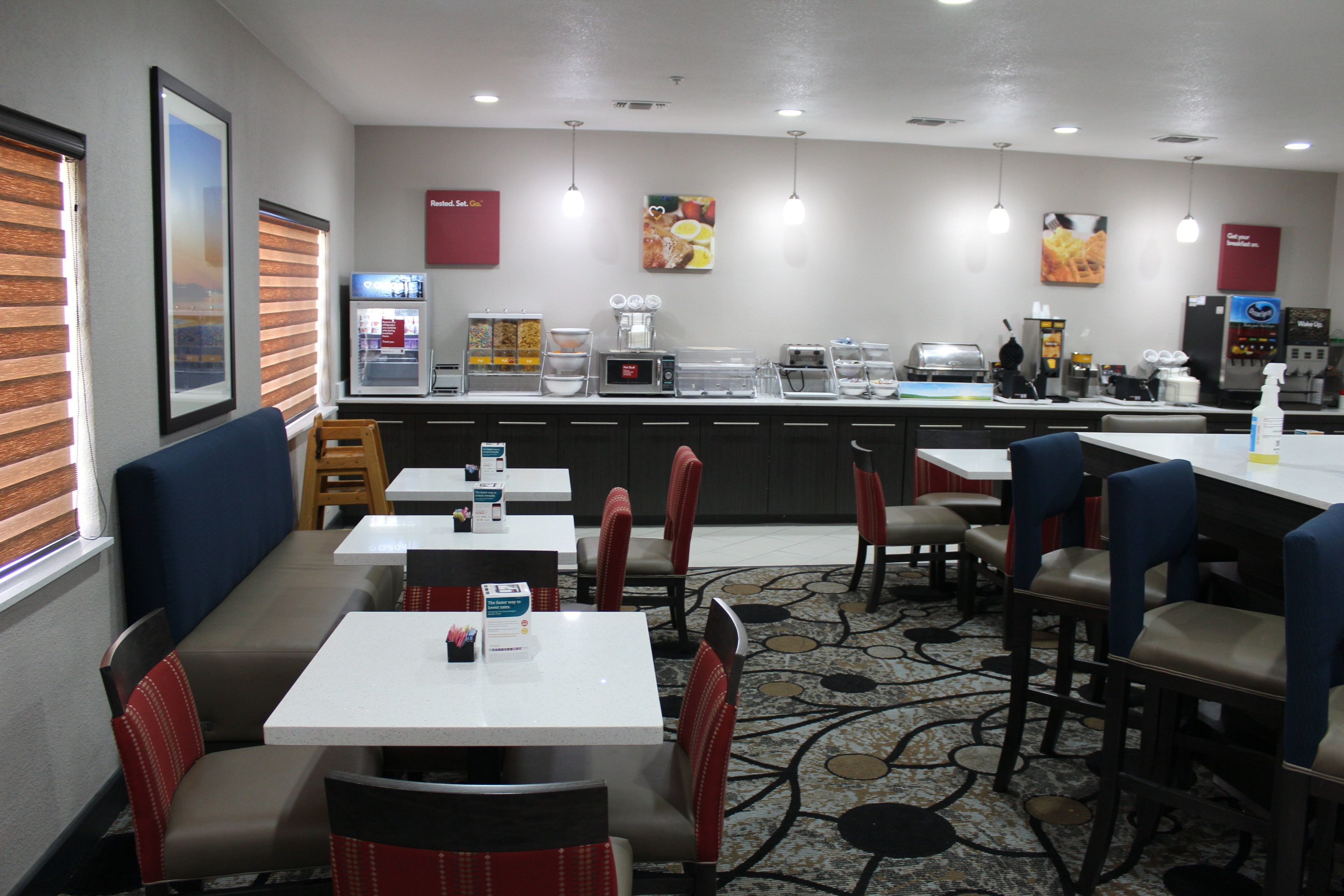 Een restaurant in een hotel met zitjes, tafels, een koffiehoek en een toonbank met etenswaren.