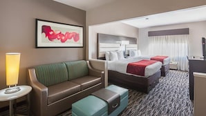A hotel room with a bed, a sofa, a small table with a lamp, a painting on the wall, and a window with curtains. - Comfort Suites Lewisville - Dallas (Lewisville)