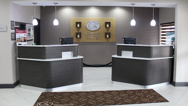 A reception area with two dark grey reception desks, a 'Comfort Suites' sign, and a patterned rug on the floor. - Comfort Suites Lewisville - Dallas (Lewisville)