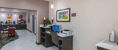 Zona de recepción de hotel con mostrador, computadora y un cuadro en la pared.