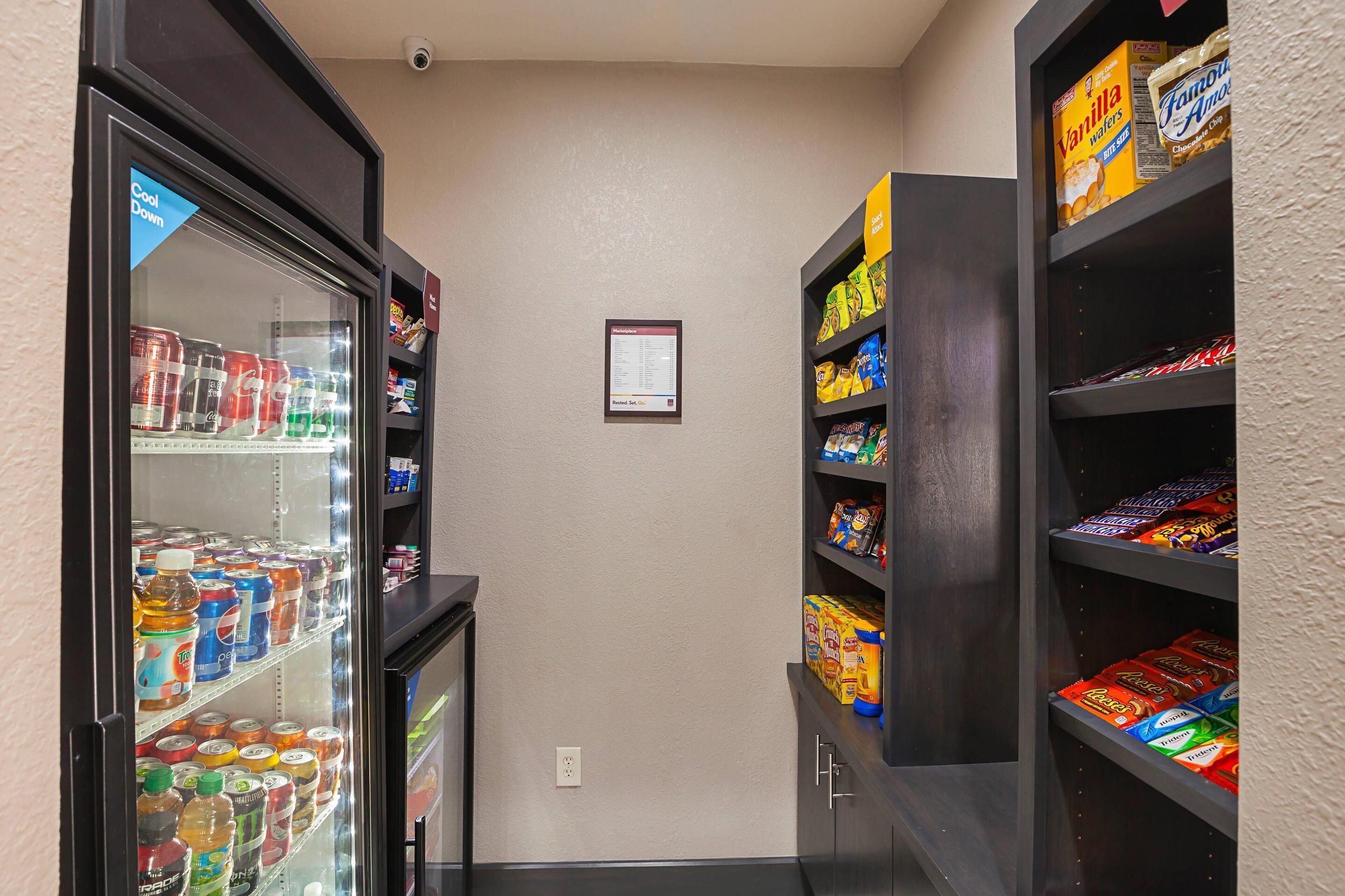 Un pasillo estrecho con un refrigerador de bebidas a la izquierda y estantes con aperitivos a la derecha.