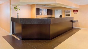 Una recepció amb un taulell fosc, un vas amb flors verdes i un televisor fixat a la paret.