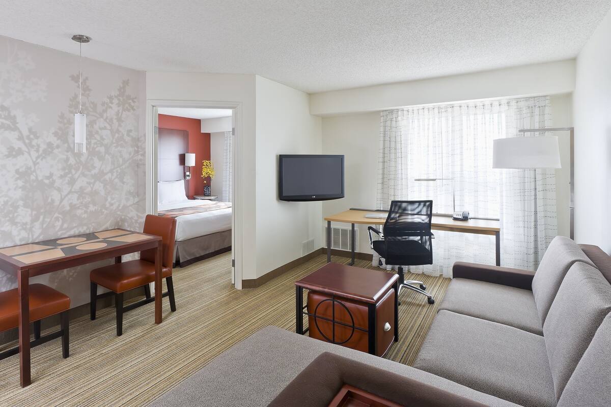 Una habitación de hotel con cama, escritorio, televisor, sofá y un comedor con sillas.