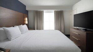 Una habitació d'hotel amb un llit gran, una televisió sobre un moble de fusta, una taula de nit amb una làmpada i una finestra amb cortines.