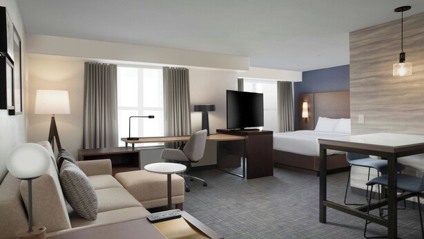 Habitació d'hotel amb un llit, escriptori amb televisió, sofà, taula petita i una cadira.