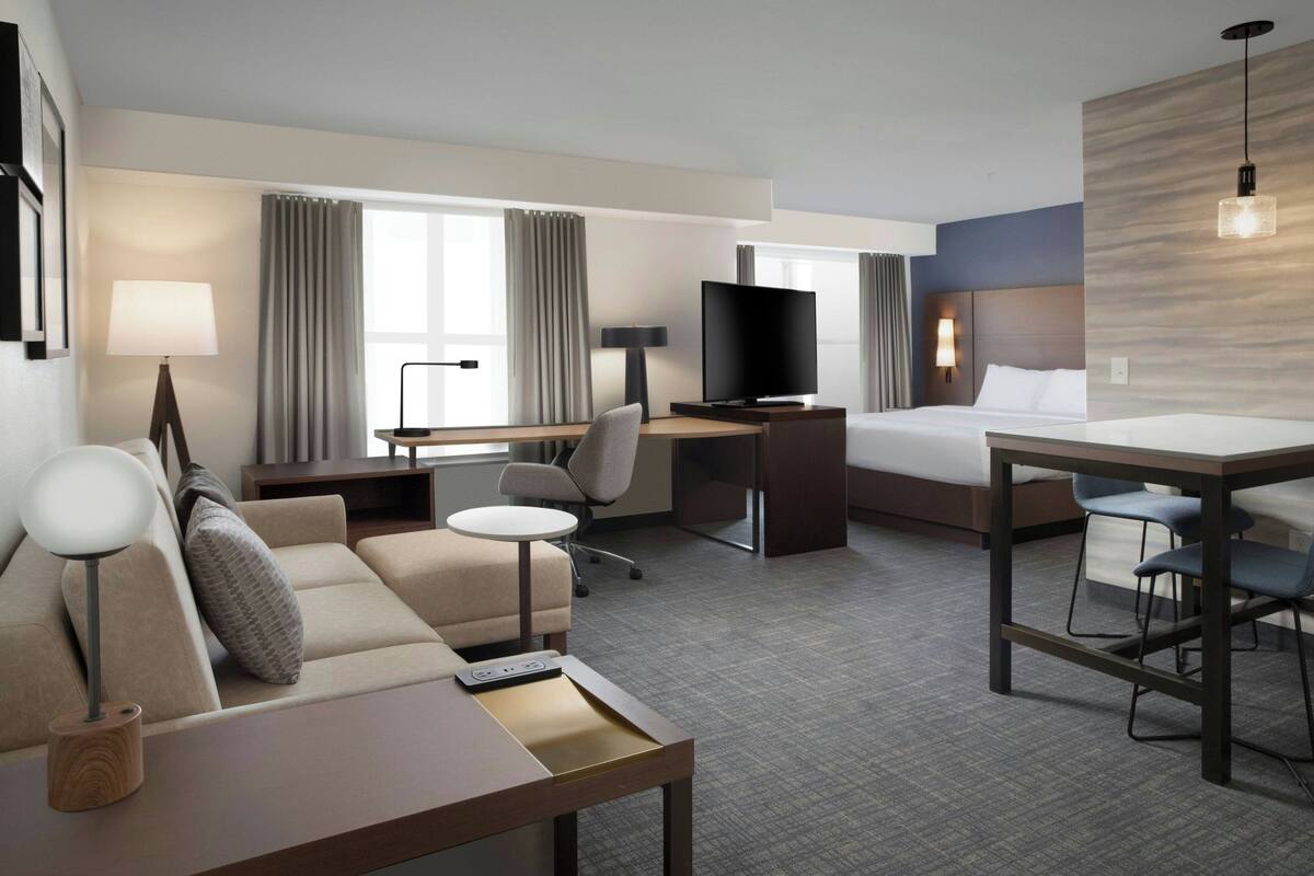 Habitación de hotel con cama, escritorio con televisor, sofá, mesita y silla.