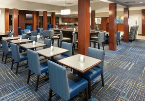 Un hall de hotel con varias zonas de estar, que incluyen mesas y sillas, y un área de cocina visible al fondo.