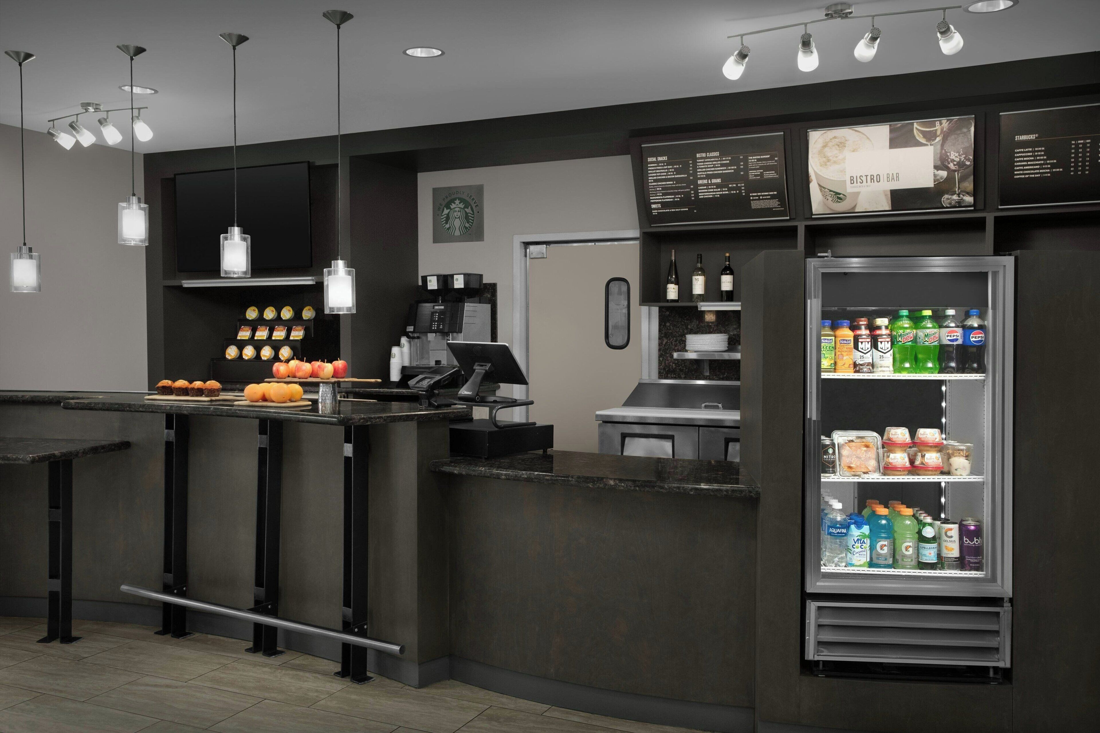 A modern bistro bar with a menu board, a beverage refrigerator stocked with drinks, and a coffee machine.