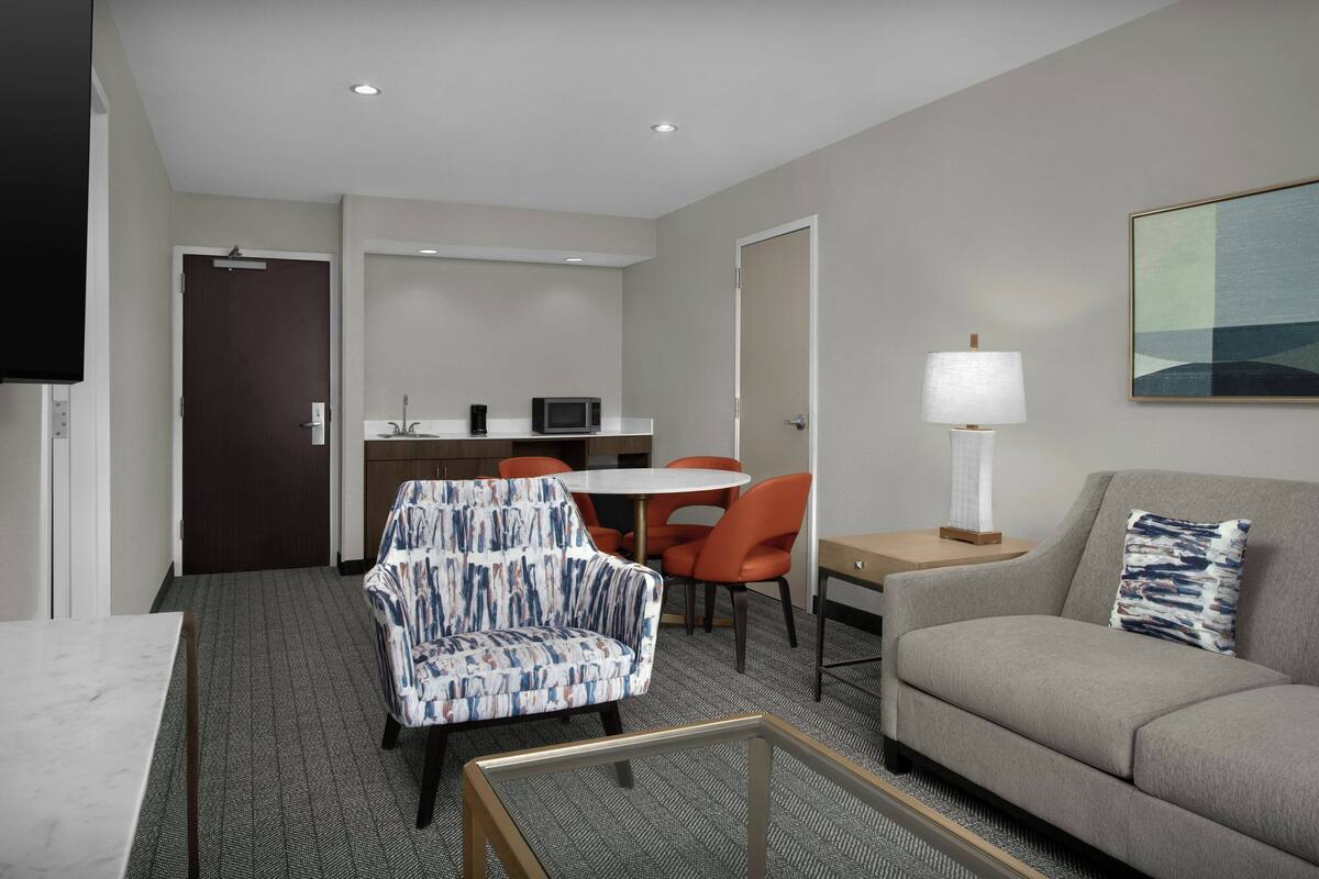 A hotel room with a sofa, a chair, a table, a lamp, and a painting on the wall.