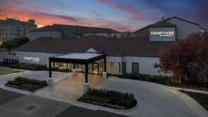 Un hotel Courtyard by Marriott con entrada cubierta, jardines ajardinados y un cielo al atardecer.