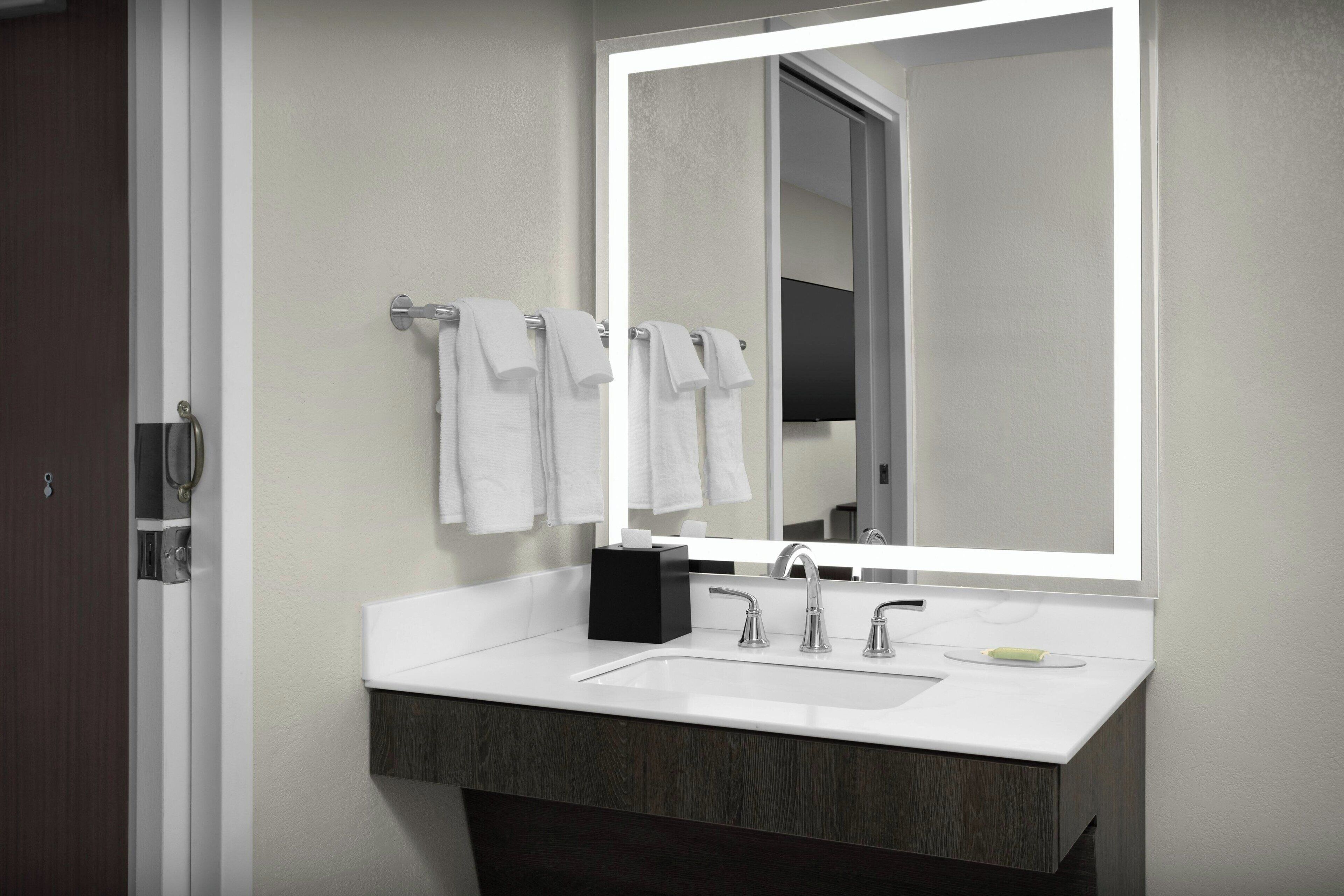 A modern bathroom with a white sink, two faucets, a large mirror, and a towel rack with white towels.