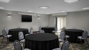 A conference room with round tables, chairs, a flat-screen TV, and recessed ceiling lights.