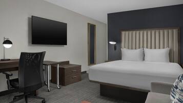 A hotel room with a bed, desk, chair, and a flat-screen TV.