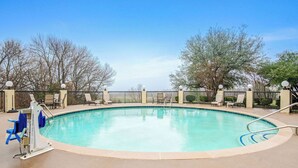 A swimming pool with a pool lift, lounge chairs, and a fence with lights.