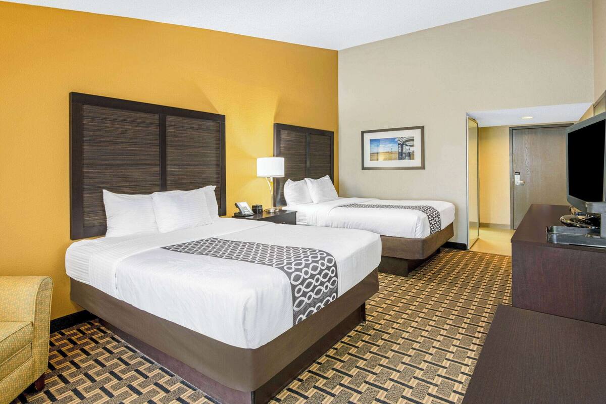 A hotel room with two beds, a sofa, a desk, and a television.