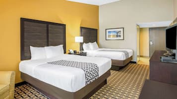 A hotel room with two beds, a sofa, a desk, and a television.