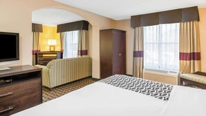 A hotel room with a bed, a desk with a TV, a wardrobe, a sofa, and a window with curtains.
