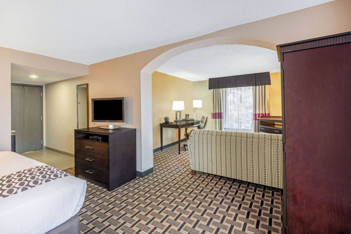 A hotel room with a bed, a desk with a computer, a TV, and a seating area with a patterned sofa.