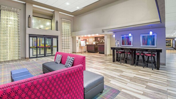 A spacious lobby with a red patterned sofa, a bar area with stools, and a large glass door leading outside.