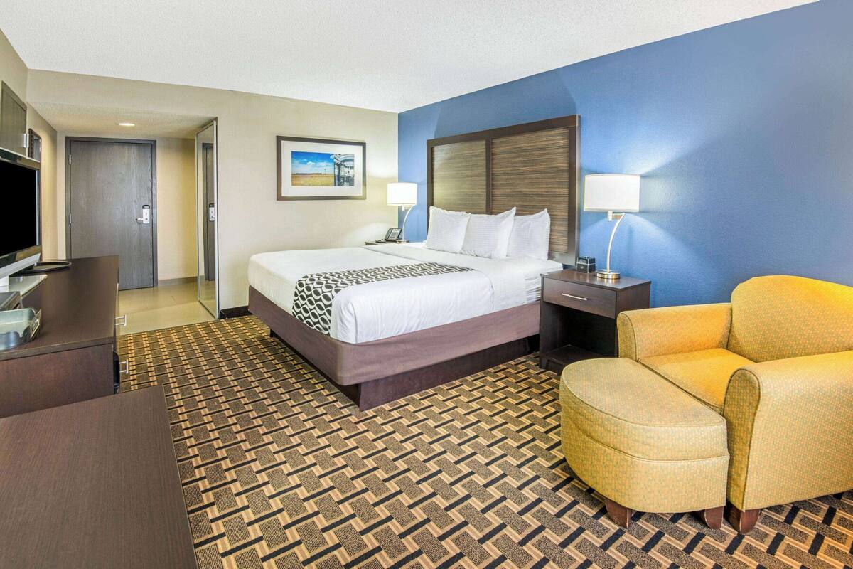 A hotel room with a bed, bedside table, lamp, chair, and a television.