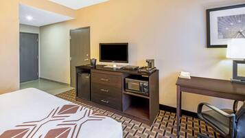 A hotel room with a bed, a desk with a computer, a microwave, and a TV.