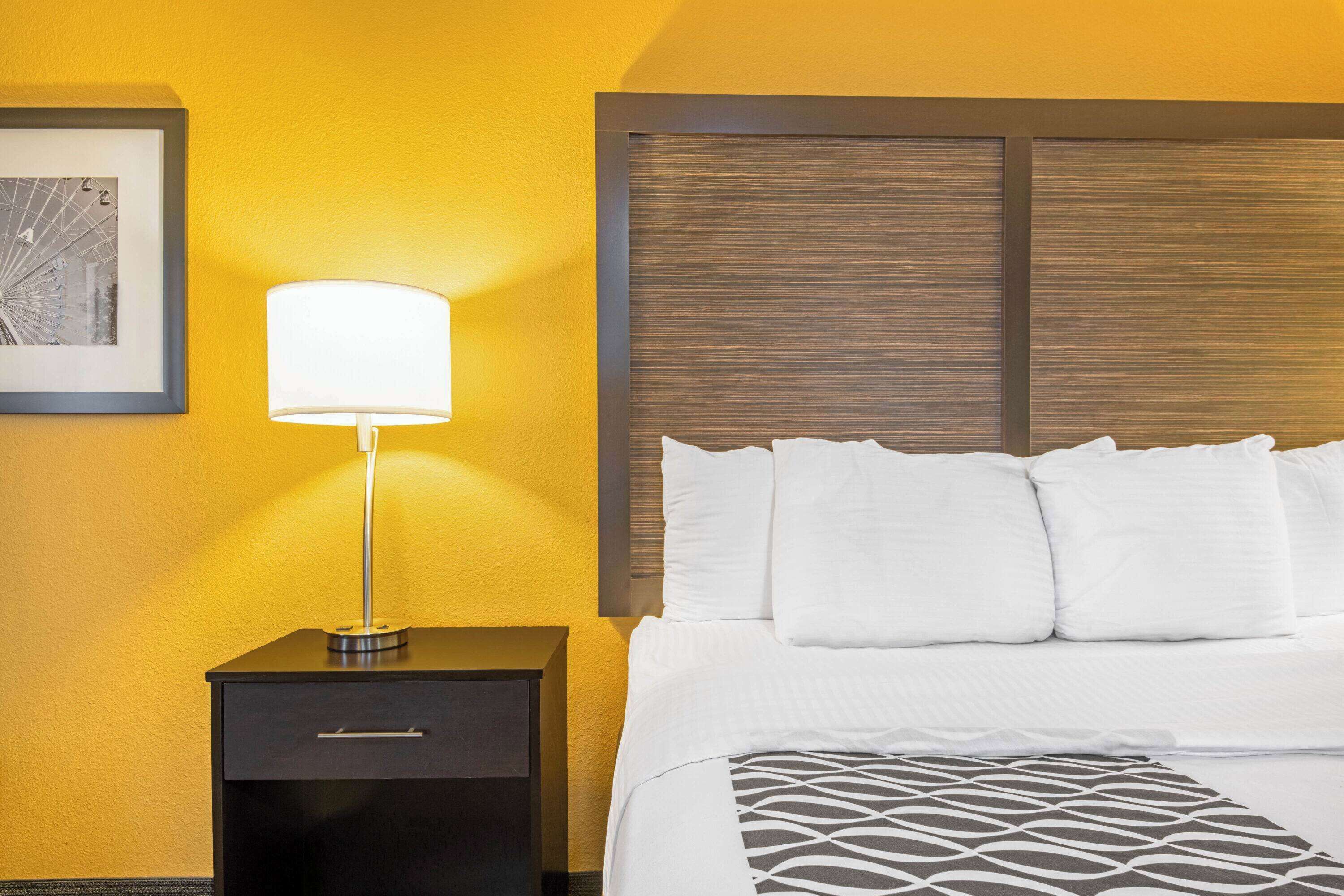 A hotel room with a bed, a nightstand, a lamp, and a framed picture on the wall.
