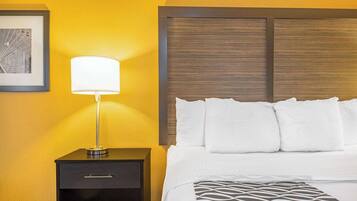 A hotel room with a bed, a nightstand, a lamp, and a framed picture on the wall.