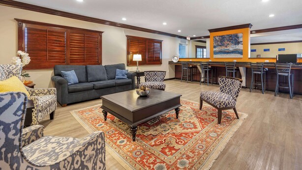 A spacious living room with a dark wooden coffee table, patterned armchairs, a grey sofa, and a red and orange patterned rug.