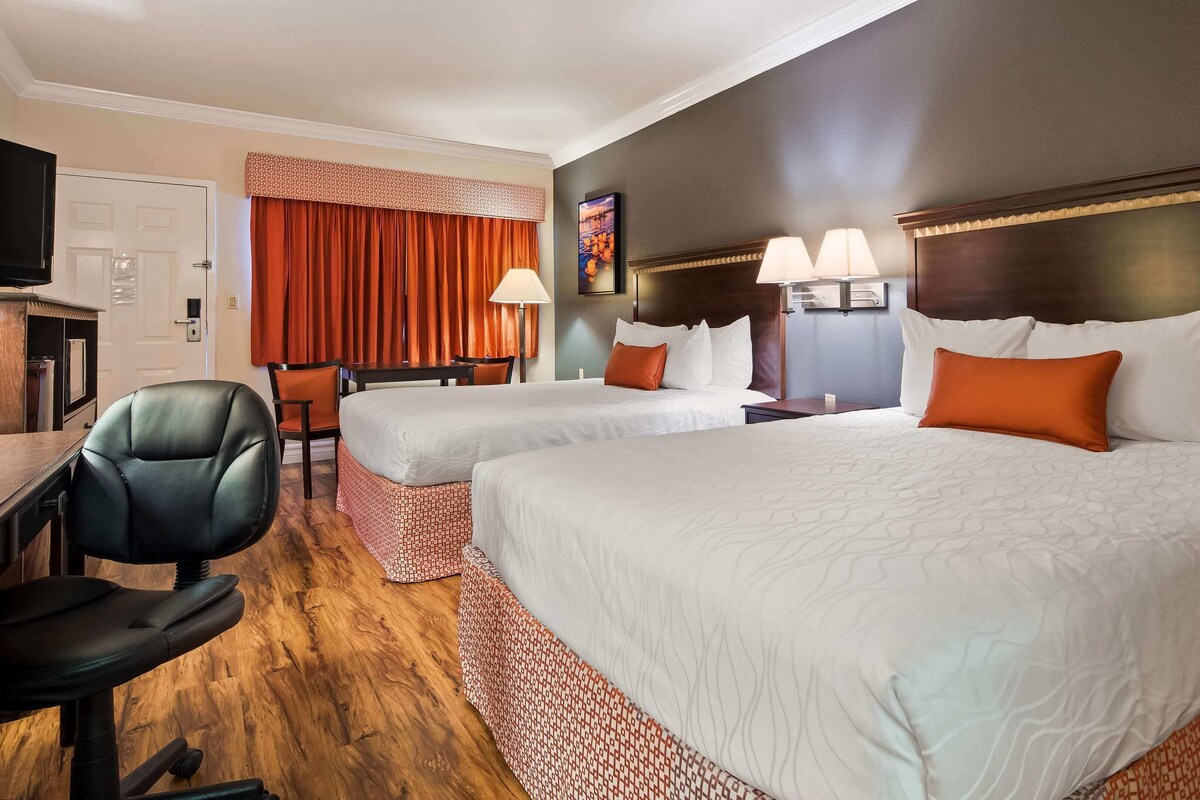 A hotel room with two beds, a desk, a chair, and a television.